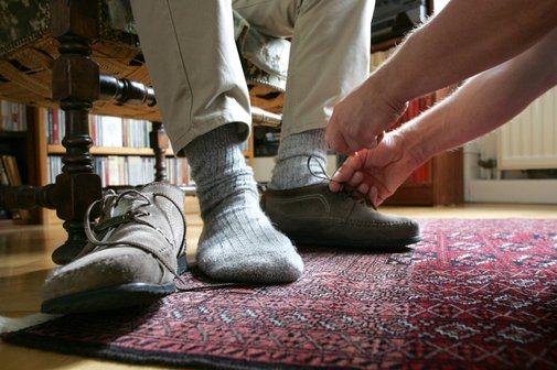 Pflege zuhause Eine Frau hilft einem Mann beim Anziehen der Schuhe