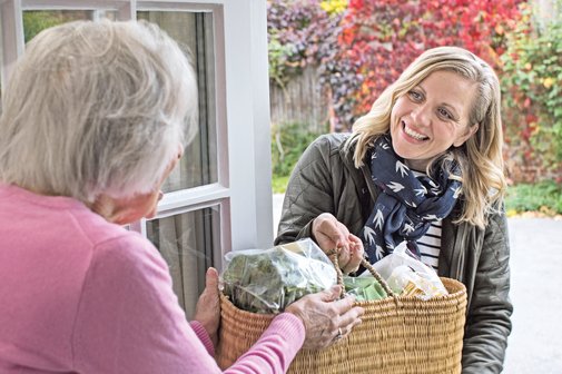 Kasse beteiligt sich an Kosten Eine Nachbarin bringt einer älteren Dame einen Korb mit Lebensmitteln.